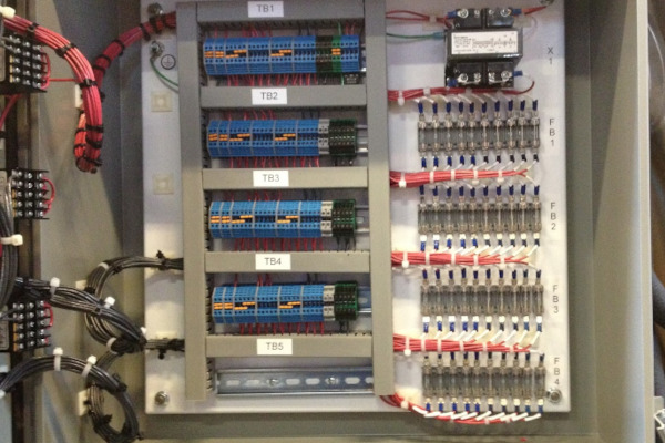 Electrical control panel with fuse blocks, terminal blocks, and transformer wiring for industrial alarm and feedback systems