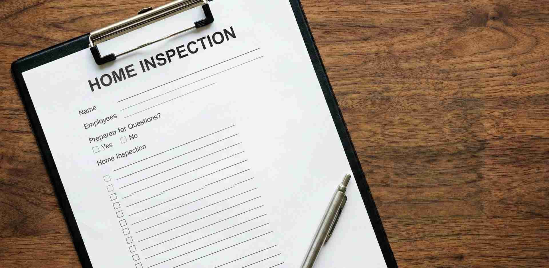 Top-down view of a home inspection checklist form on a black clipboard with a silver pen, resting on a wooden table surface.
