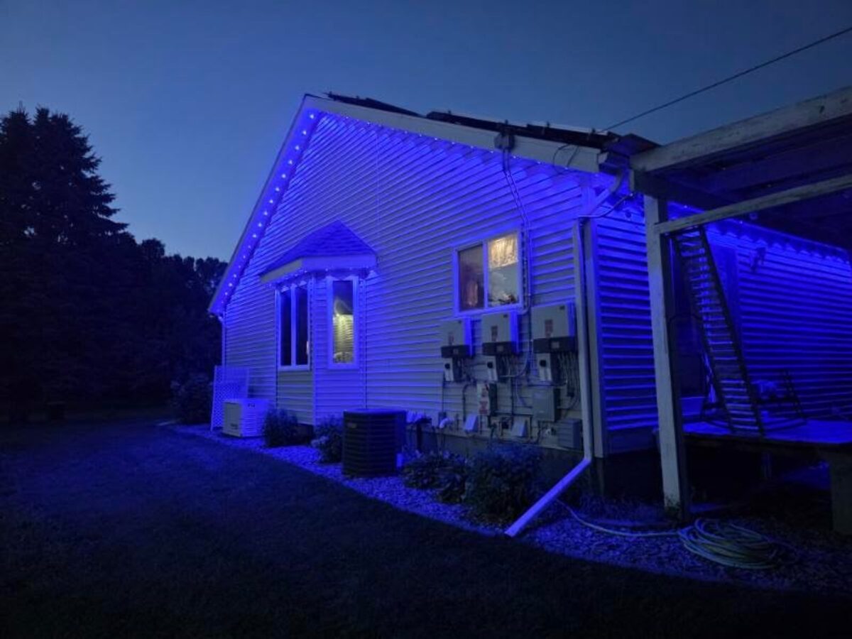 Home exterior lit in blue by under-eave addressable LED puck lights at dusk