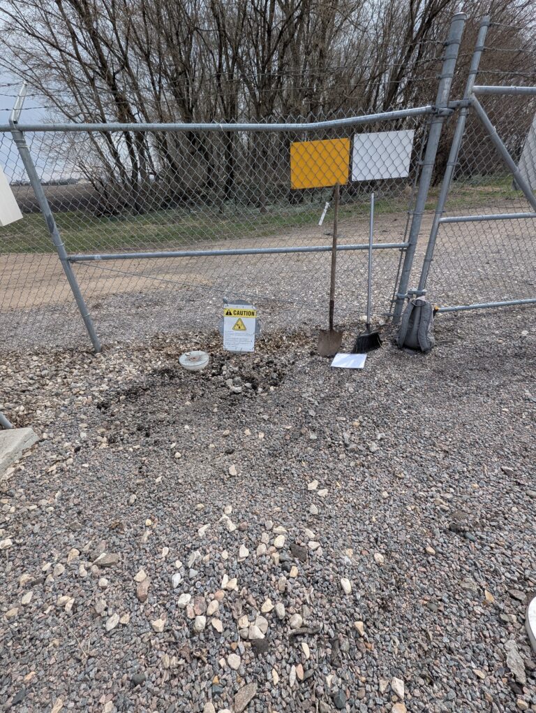 Cell tower compound in Olivia, Minnesota after temporary electrical service removal — conduit excavated, site clean, gate secured